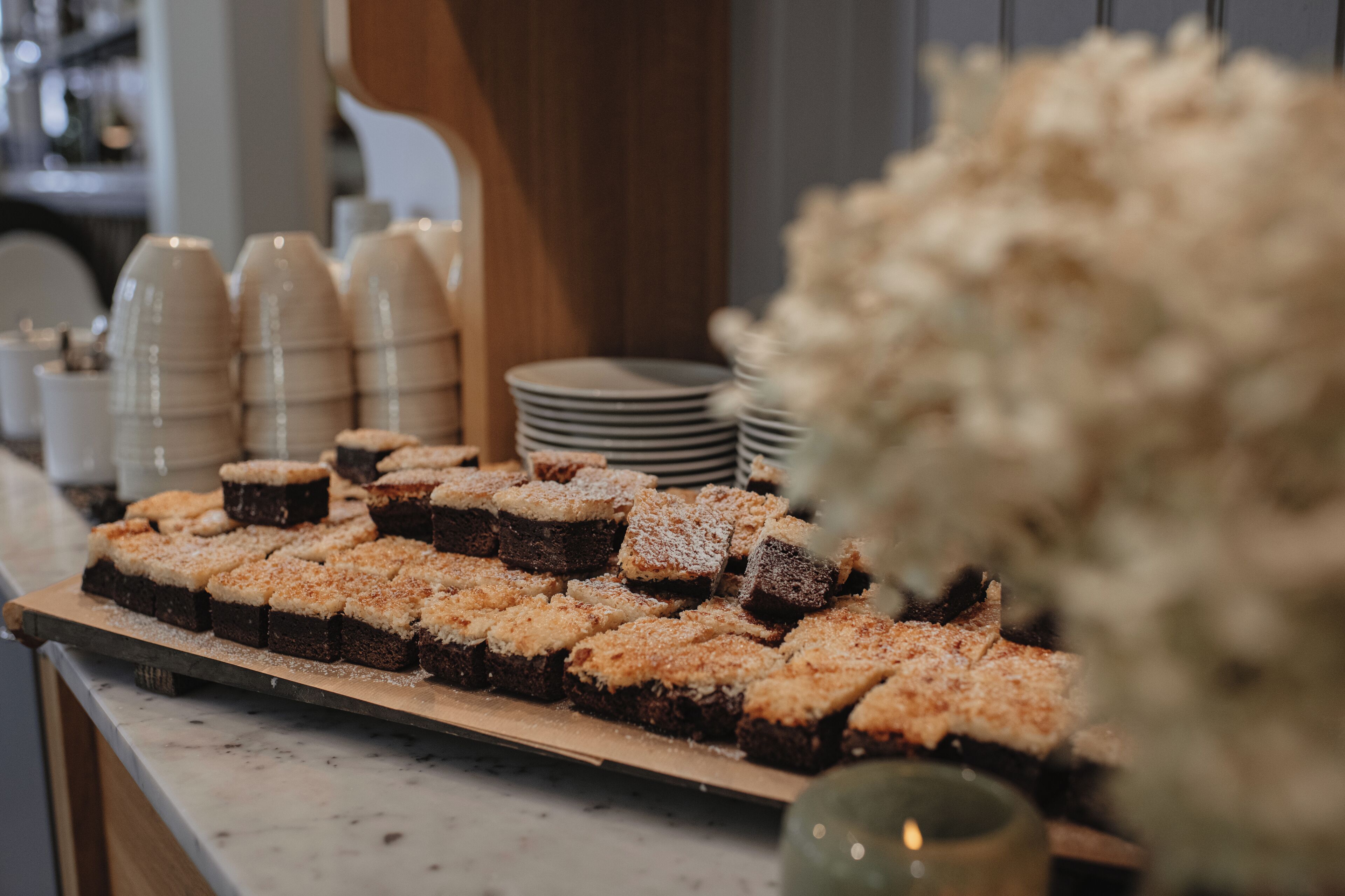 A counter with a variety of desserts, including brownies and other baked goods, with stacks of plates and cups in the background.