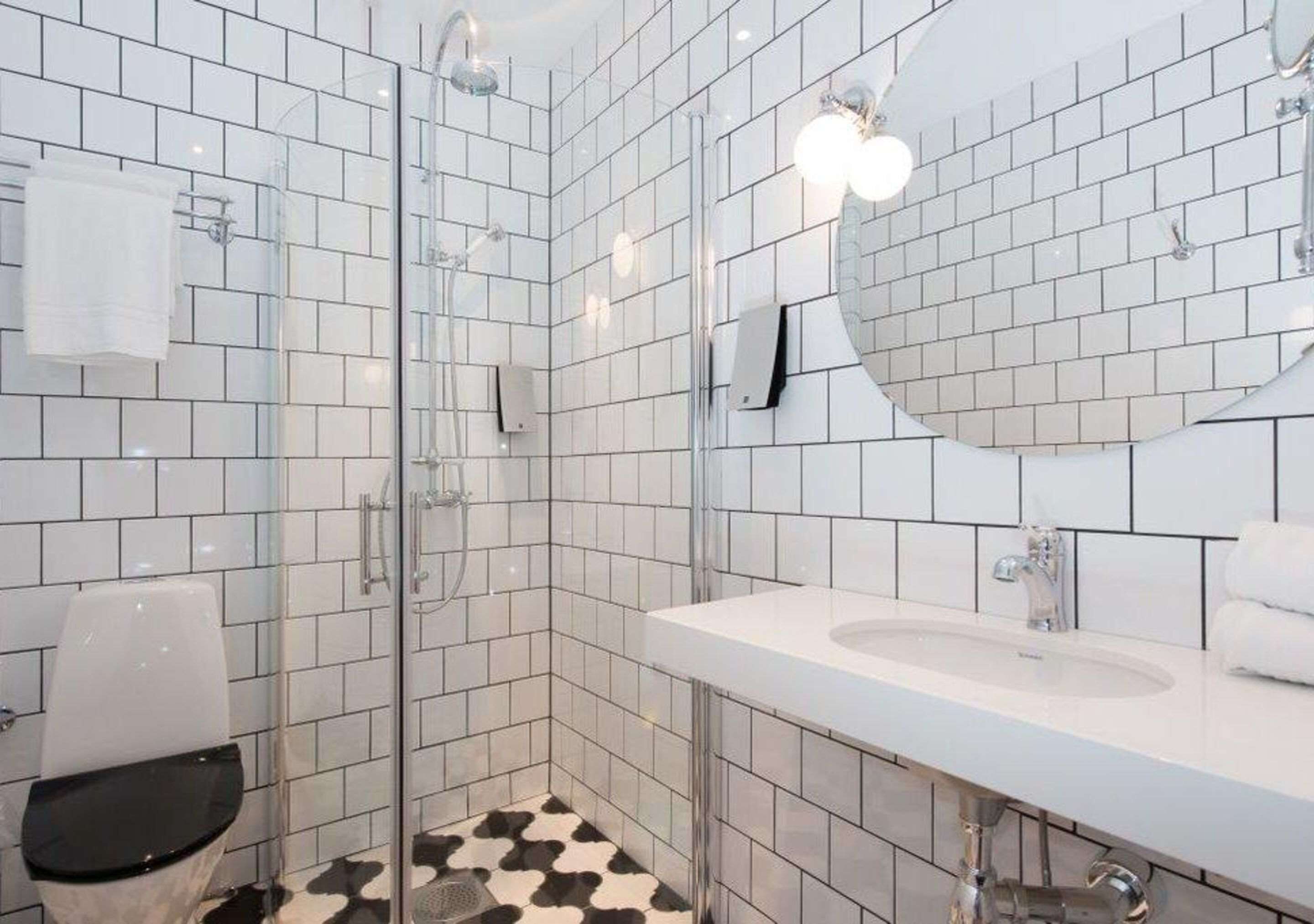 Een moderne badkamer met witte betegelde wanden, een glazen douchecabine, een wit wastafelmeubel en een vloer met een zwart-wit patroon.
