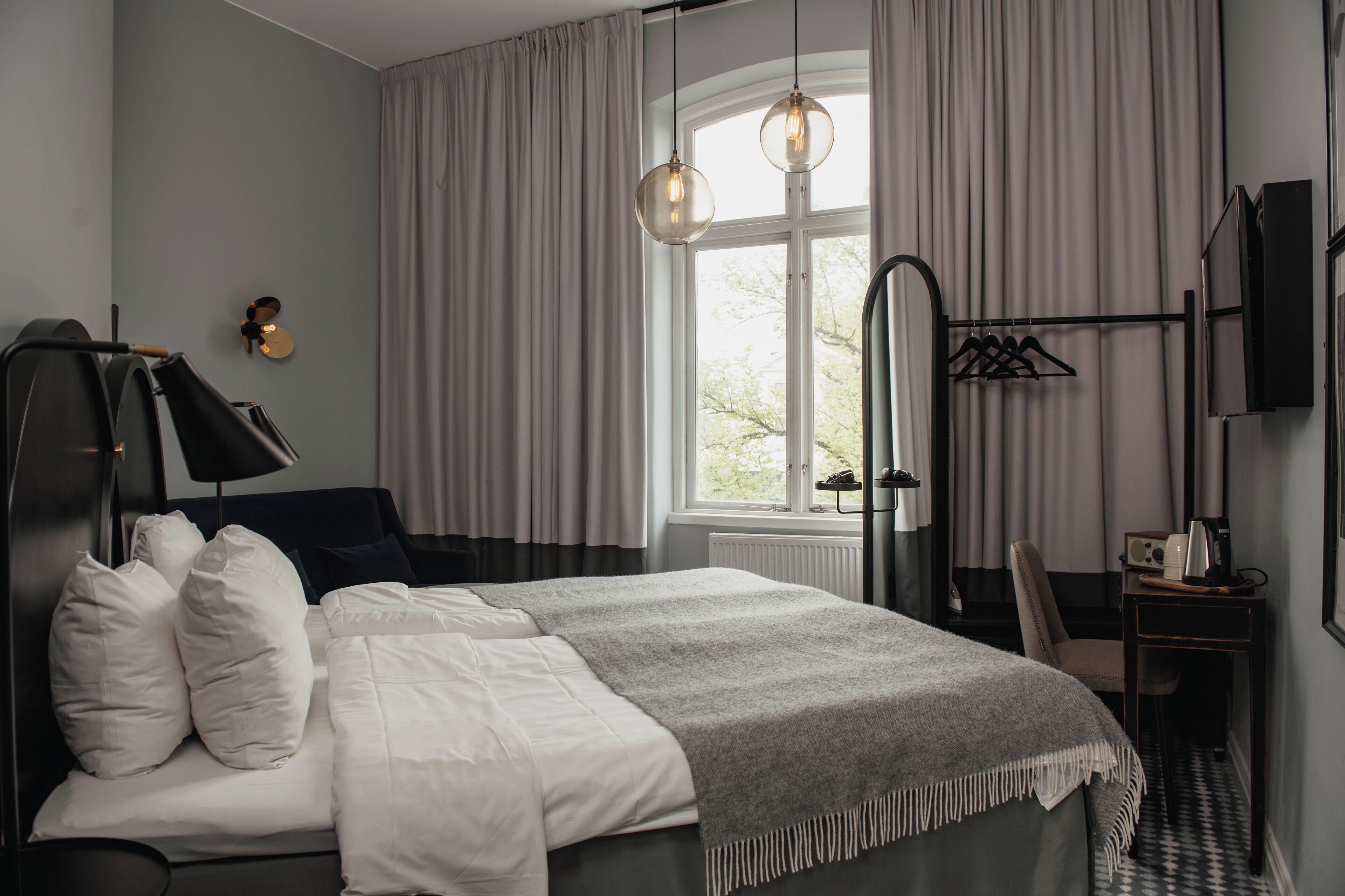 Un dormitorio moderno con cama, mesita de noche, lámpara y vistas al exterior a través de una ventana.