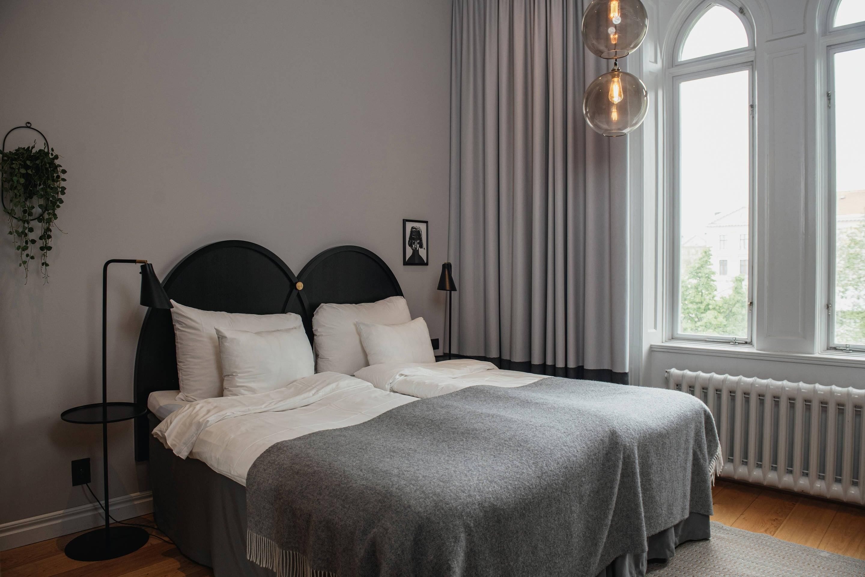 A bedroom with a bed, a floor lamp, a radiator, and a window with curtains.