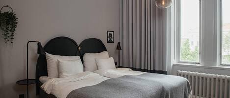 A bedroom with a bed, a floor lamp, a radiator, and a window with curtains.