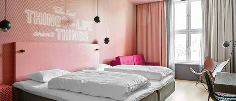 Un dormitorio moderno con cama, pared rosa con una cita motivacional, ventana con cortinas y una silla.