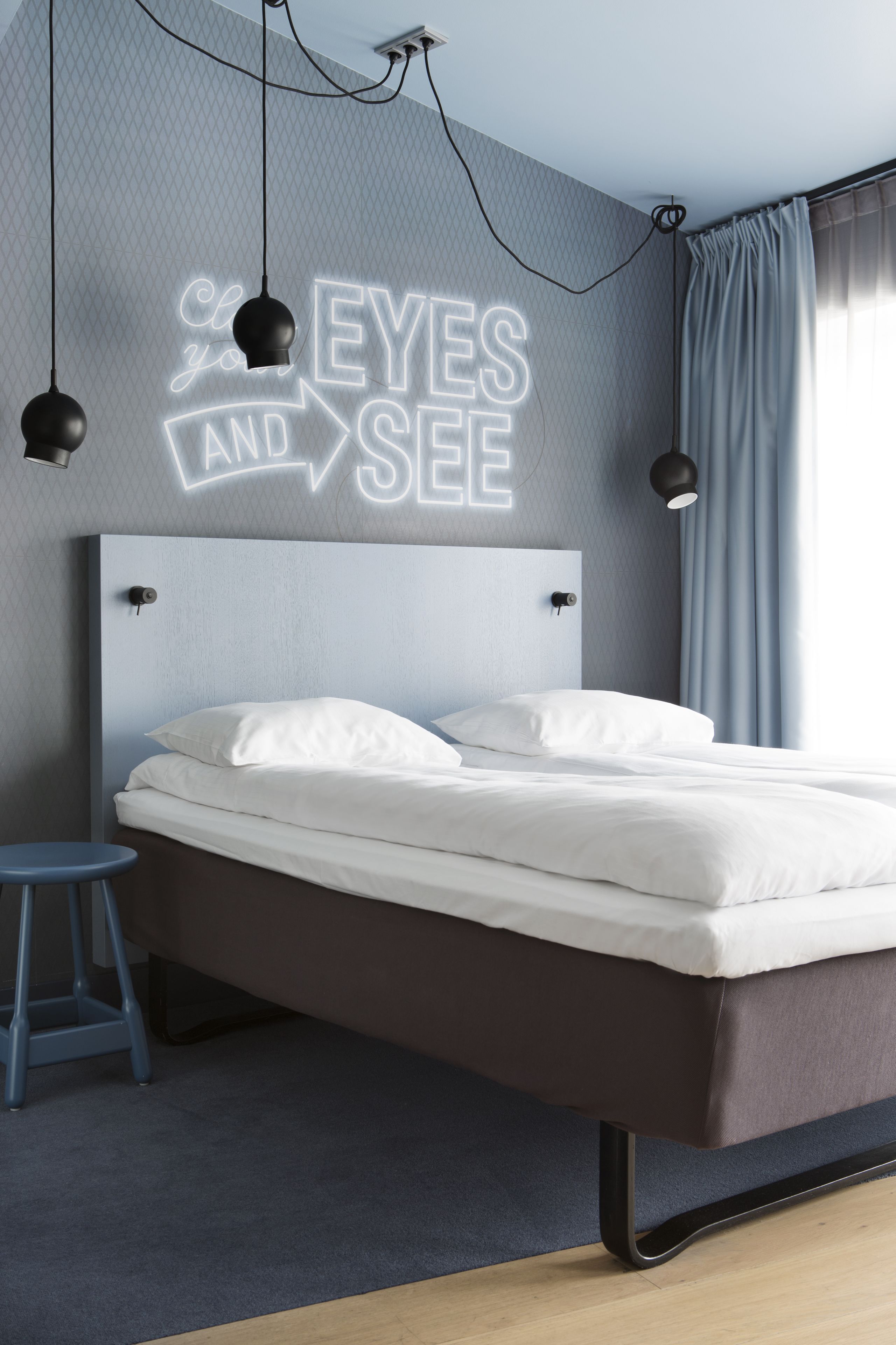 Une chambre à coucher moderne avec un lit, une table de chevet, un tabouret et un néon mural.