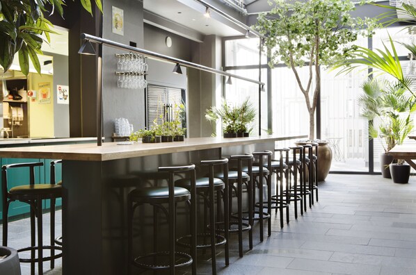 A modern bar area with high stools, a counter, and potted plants.