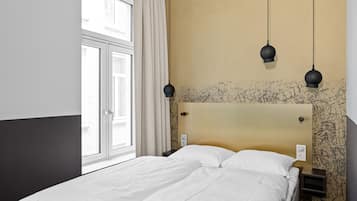A hotel room with a large bed, a window with curtains, and a wall with graffiti.