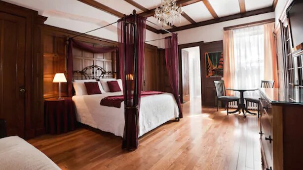 Une chambre à coucher avec un lit à baldaquin, un plancher en bois et un lustre.