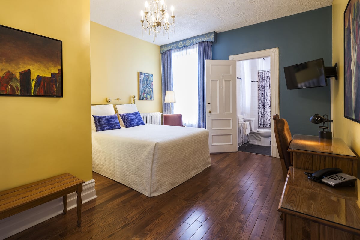 Una habitación de hotel con una cama grande, un escritorio con teléfono, una banca, una araña y un cuadro en la pared.