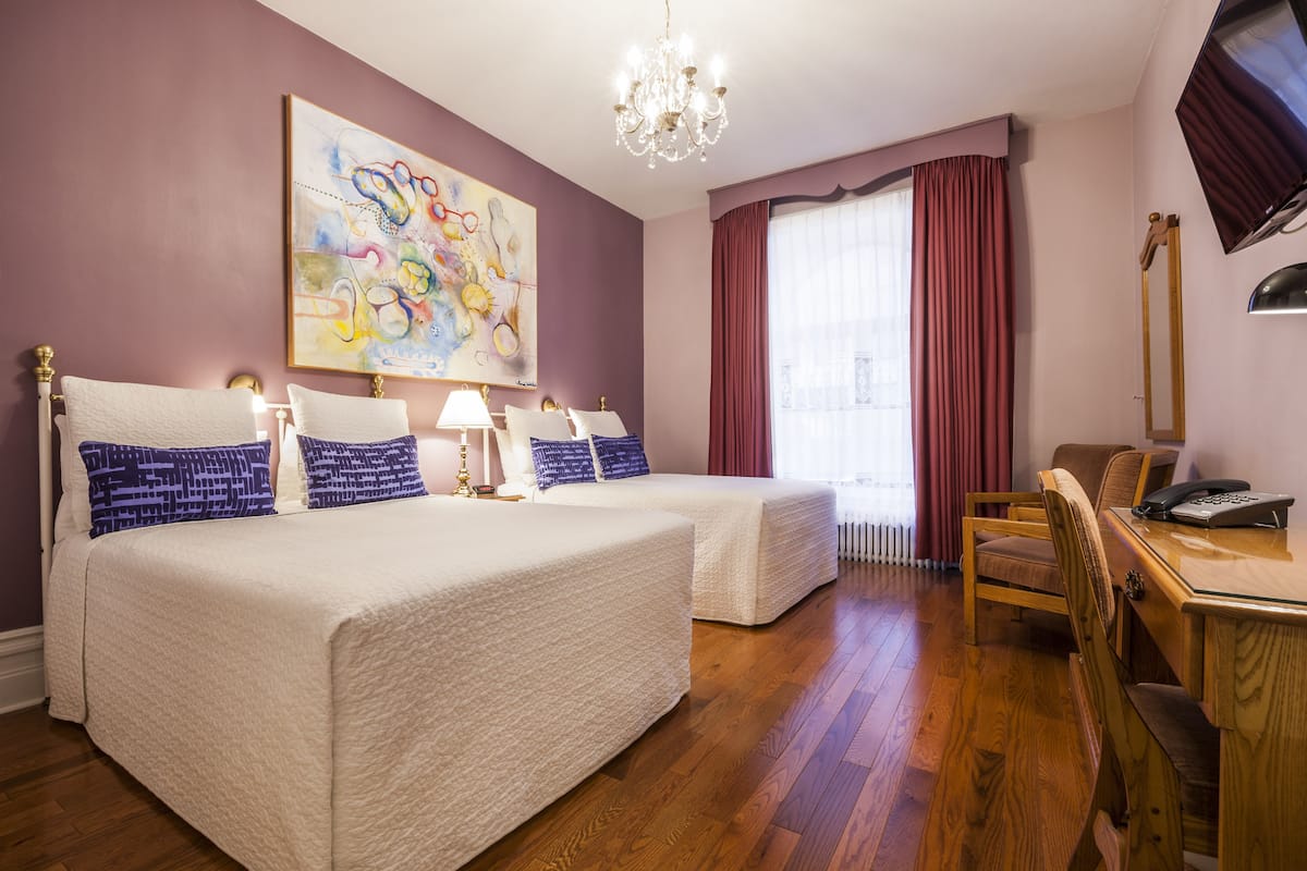Habitación de hotel con dos camas, un escritorio con teléfono, una silla, una araña y un cuadro abstracto grande en la pared.
