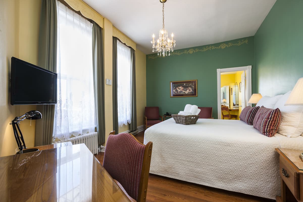 Habitación de hotel con una cama grande, un escritorio con lámpara, televisión y una araña.