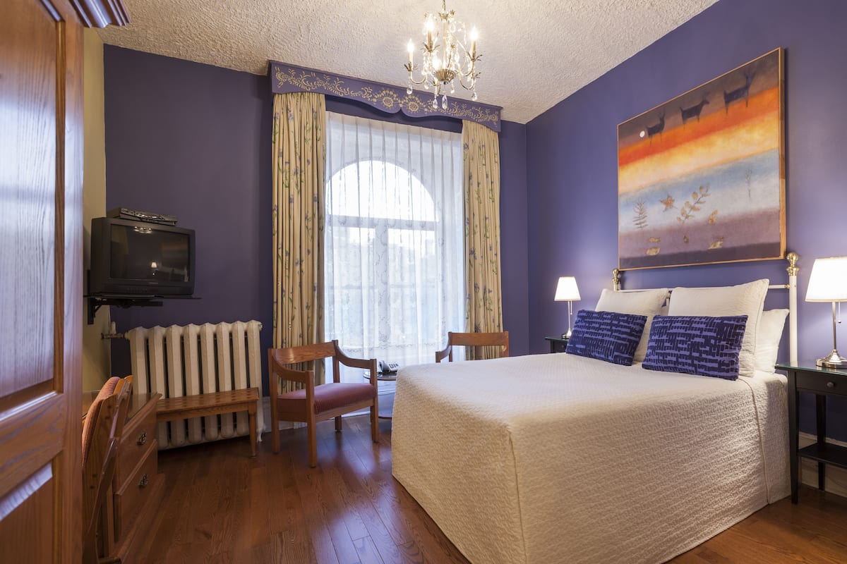 Una habitación de hotel con una cama, televisión, escritorio, silla y un cuadro en la pared.