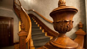 Un escalier en bois, doté d’une balustrade et orné d’une urne décorative au sommet.
