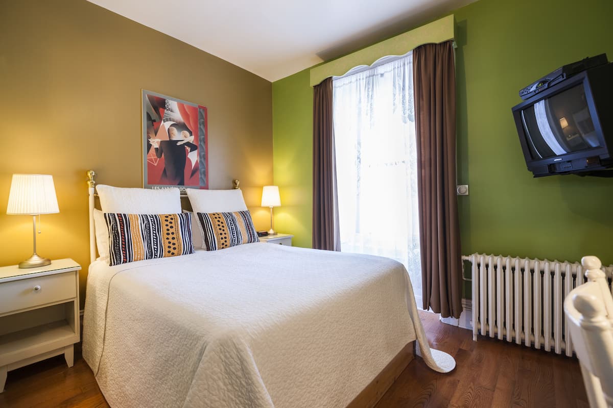 Habitación de hotel con una cama grande, dos mesitas de noche con lámparas, un televisor en la pared y una ventana con cortinas.