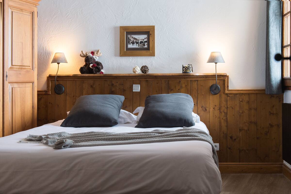 Un dormitorio con cabecera de madera, dos lámparas de noche, un cuadro enmarcado y un peluche en la mesita de noche.