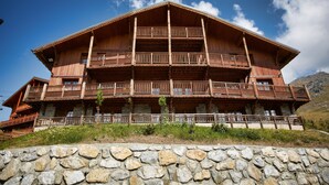Un chalet grande de madera con varios balcones, base de piedra y montañas al fondo.