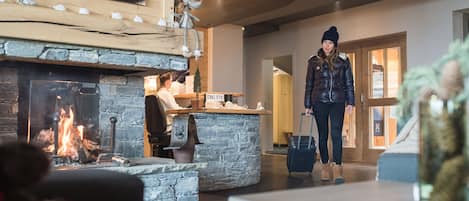 A lobby with a stone fireplace, a reception desk, and a person with luggage.