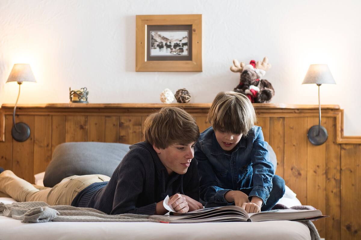 Dos personas leyendo un libro en una cama en una habitación con paneles de madera y un cuadro en la pared.