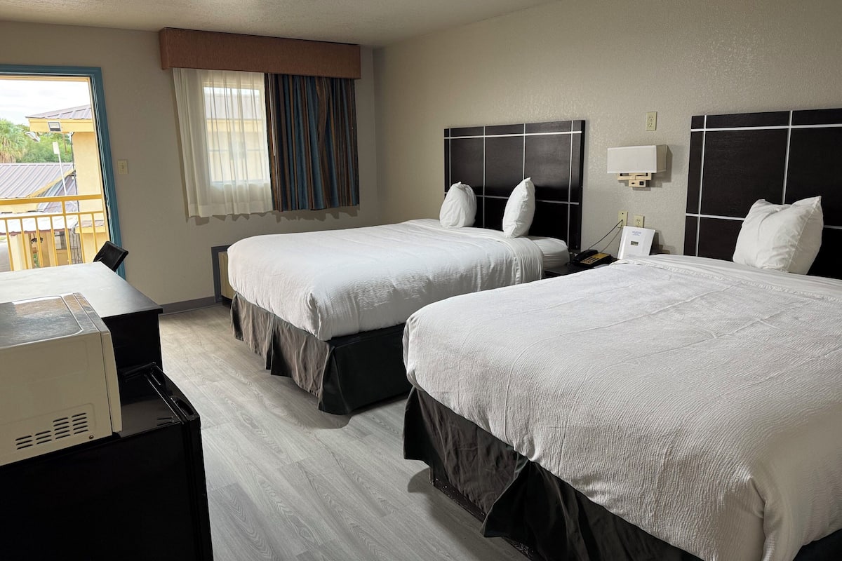A hotel room with two beds, a desk, and a window with curtains.