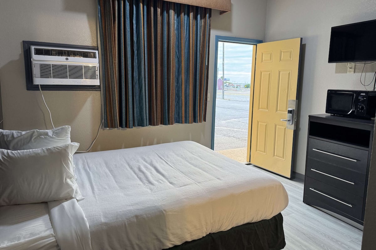 A hotel room with a bed, an air conditioning unit, a television, and a door leading outside.