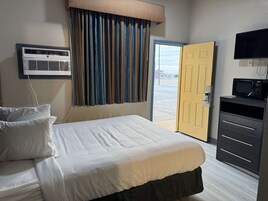 Habitación de hotel con cama, equipo de aire acondicionado, televisor y puerta que da al exterior.