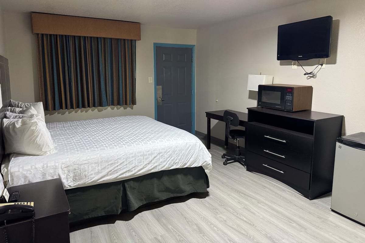 A hotel room with a bed, a desk with a microwave, a TV, and a door.