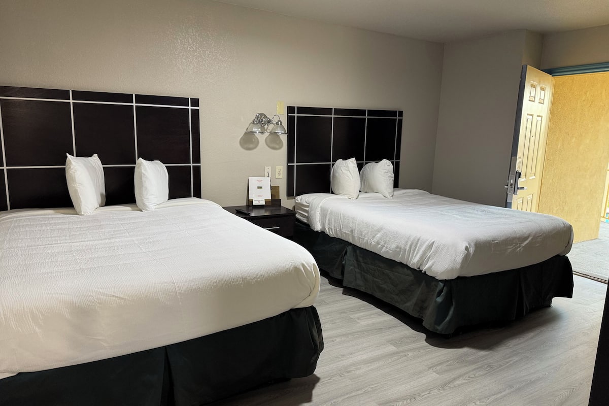 A hotel room with two beds, a nightstand, a lamp, and a door.