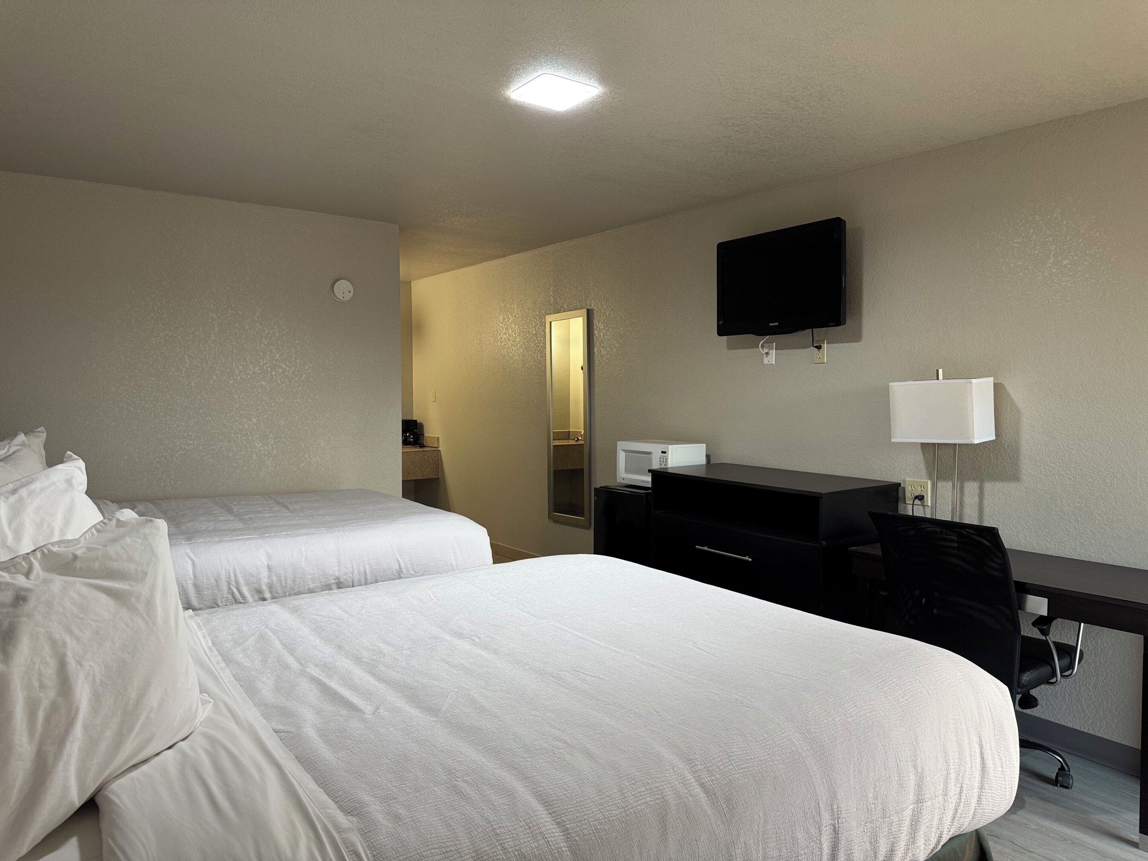 Habitación de hotel con dos camas, un escritorio, una silla, un televisor de pantalla plana, un microondas y una lámpara de noche.