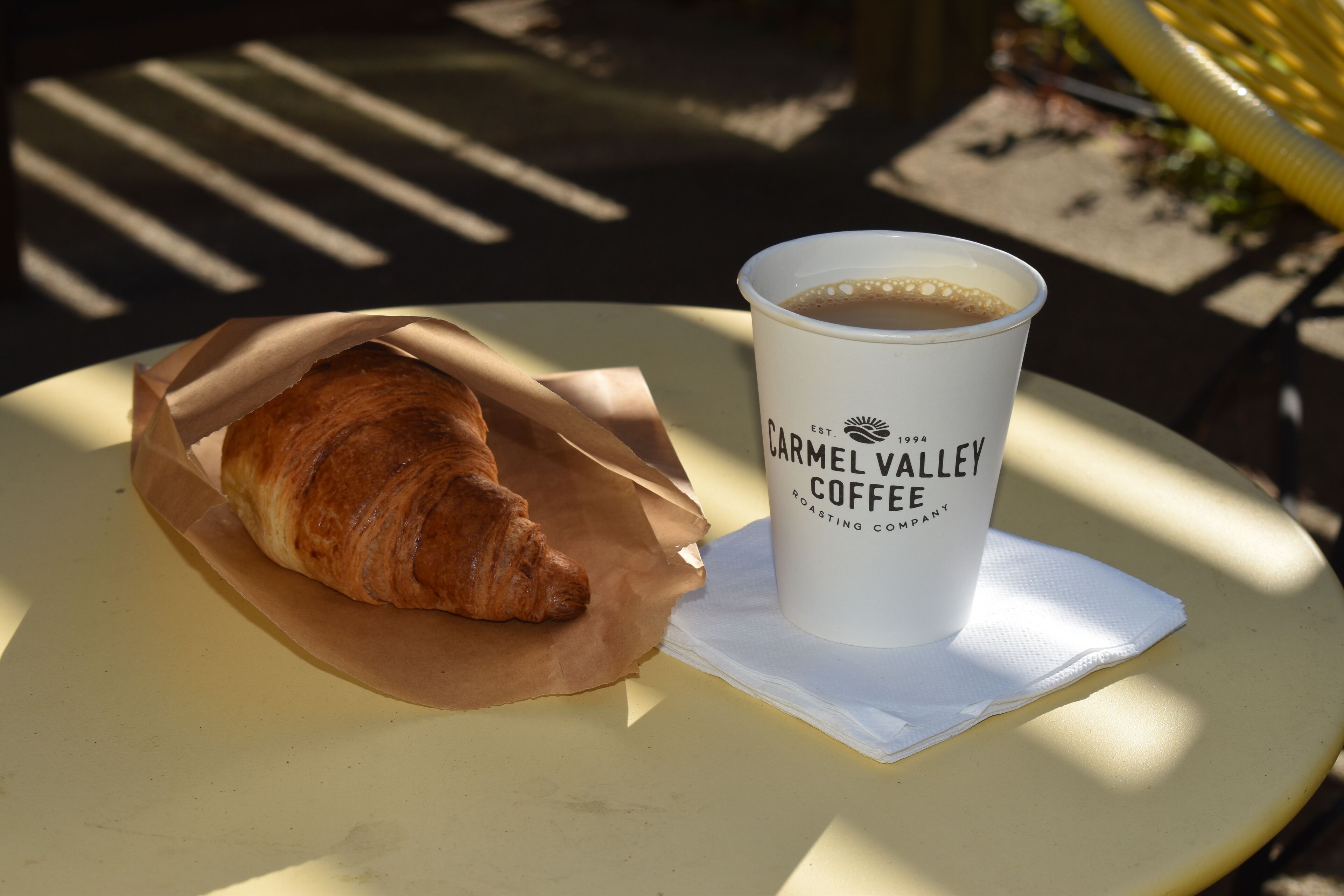 A croissant in a paper wrapper and a coffee cup with text on a table.