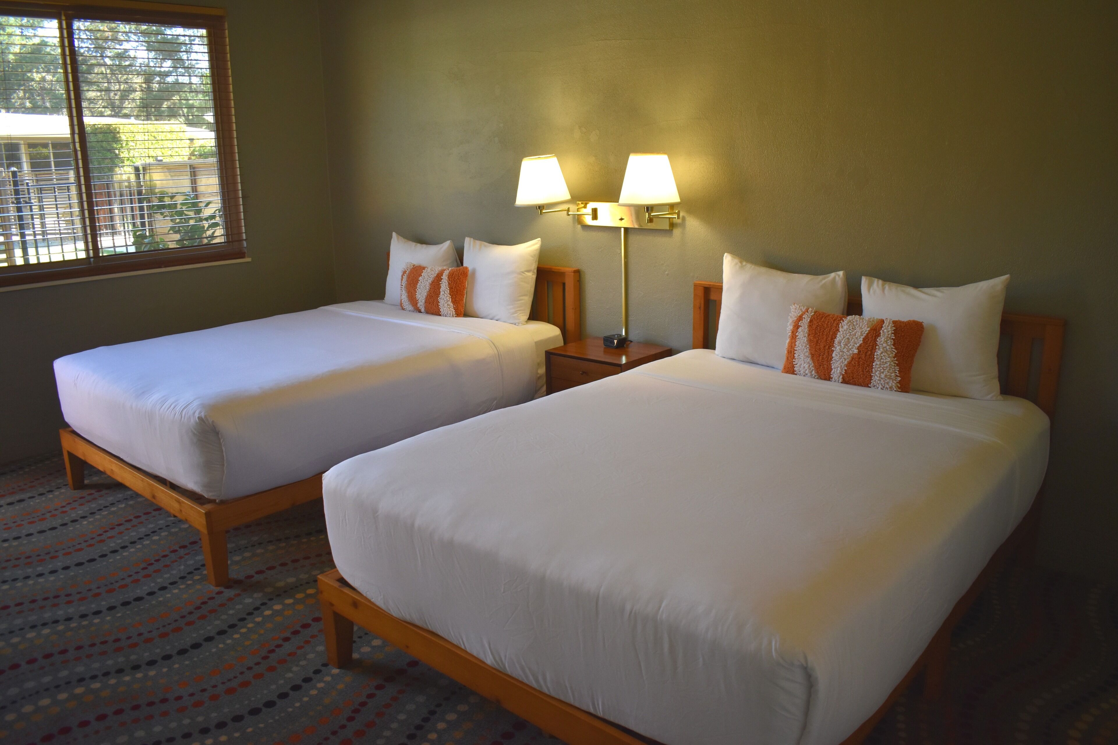 A hotel room with two single beds, a nightstand with lamps, and a patterned carpet.