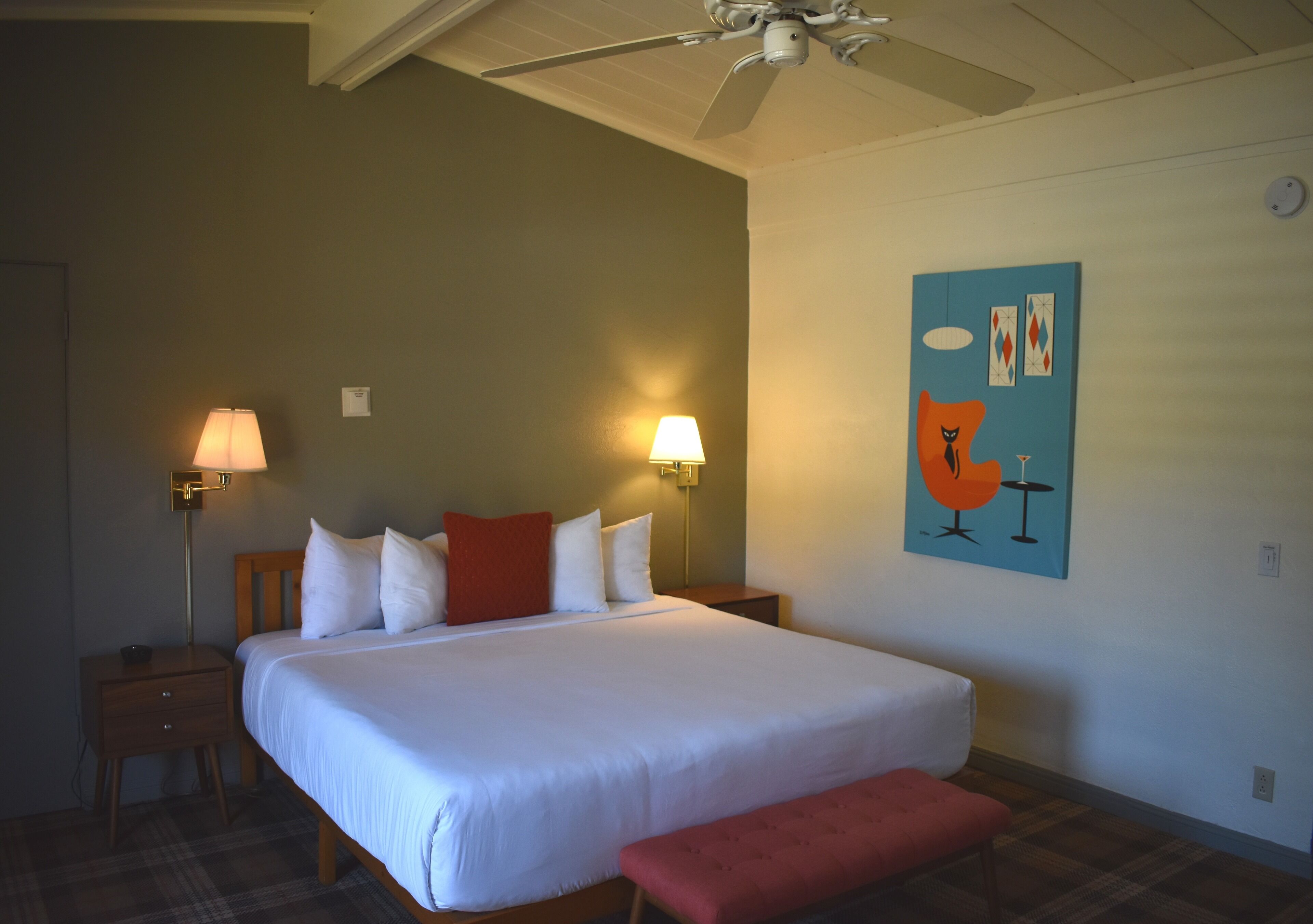 Een slaapkamer met een groot bed, twee bedlampen, een plafondventilator en een schilderij aan de muur.