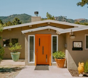 A house with a distinctive orange door, a small porch, and a view of hills in the background.