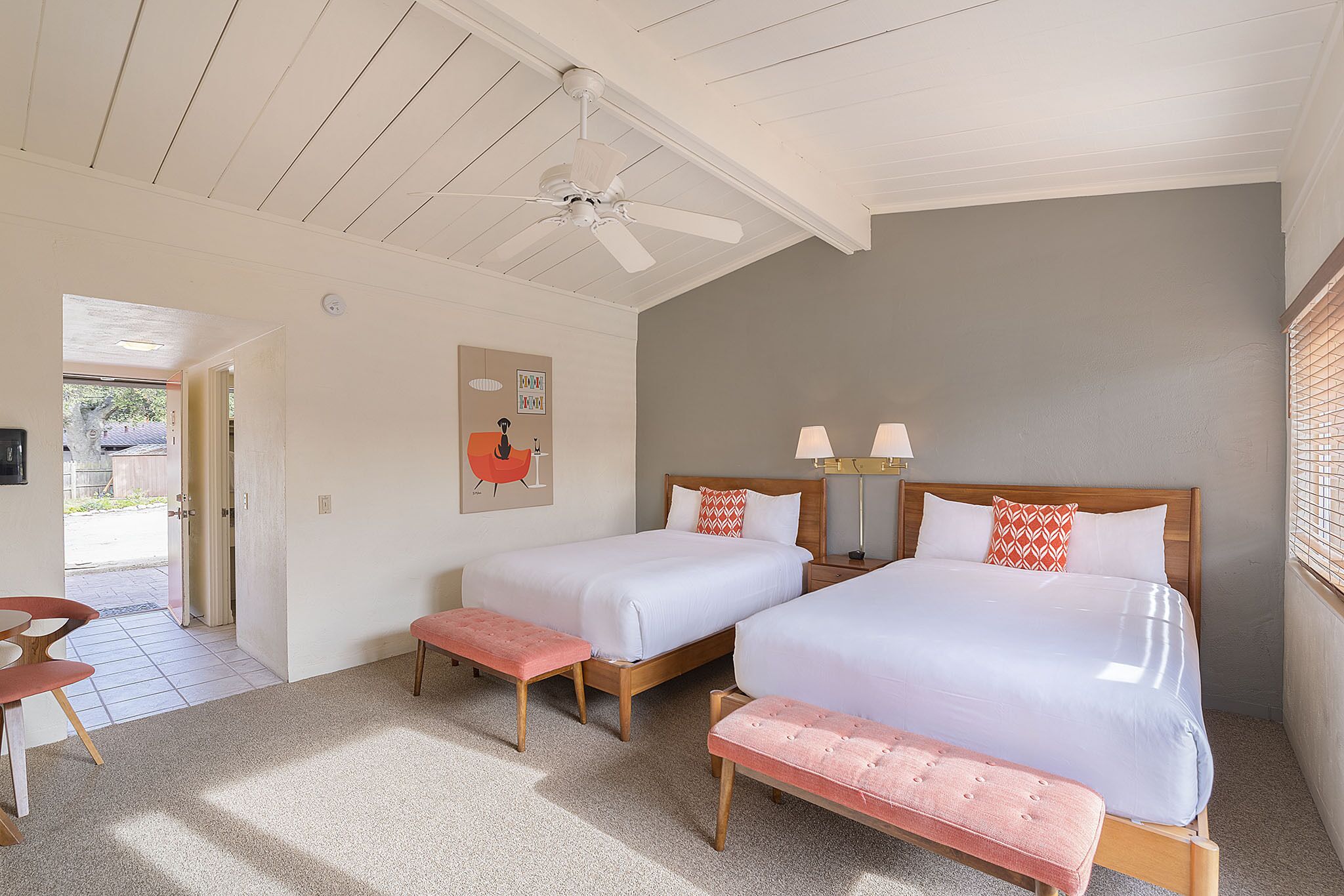 A bedroom with two beds, a ceiling fan, and a bench.