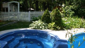 A hot tub in a backyard with a white fence, a shed, and various plants.