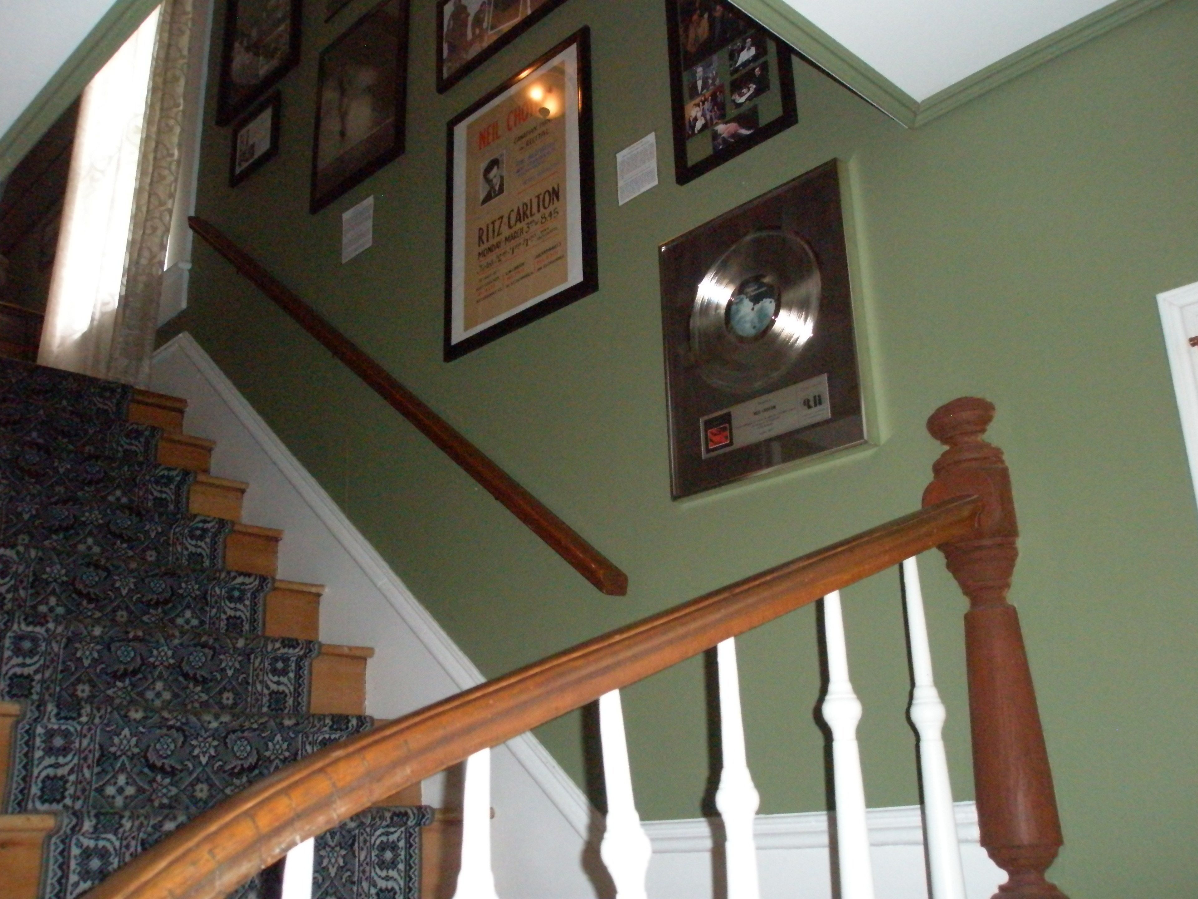 Una scala con un tappeto decorato, una ringhiera in legno e una parete con quadri e un disco in vinile.