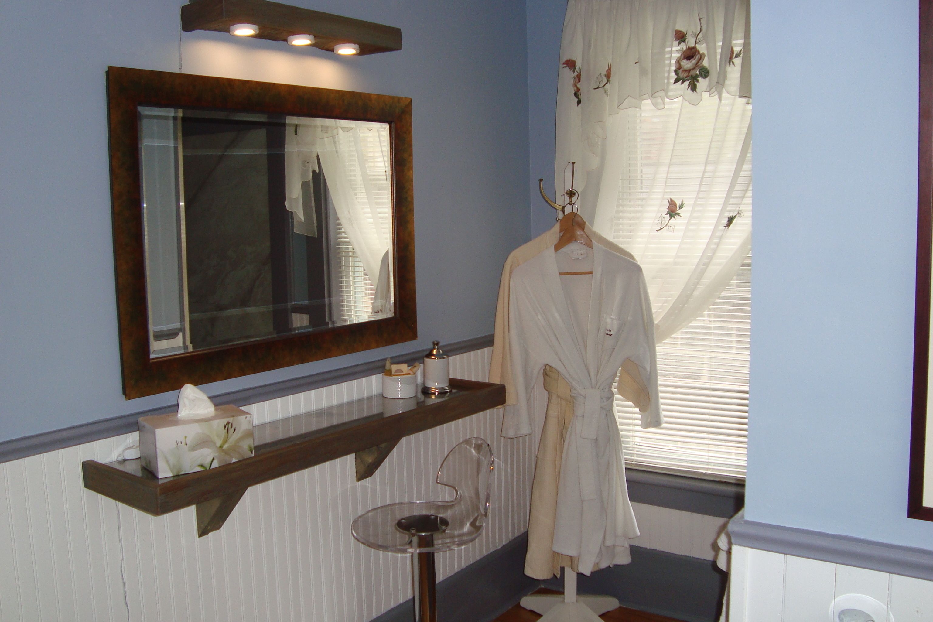 Une salle de bain avec un miroir, un porte-peignoir, une boîte de mouchoirs et un petit lavabo.