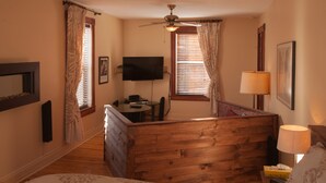 A bedroom with a wooden bed, a desk, a TV, and a window with curtains.