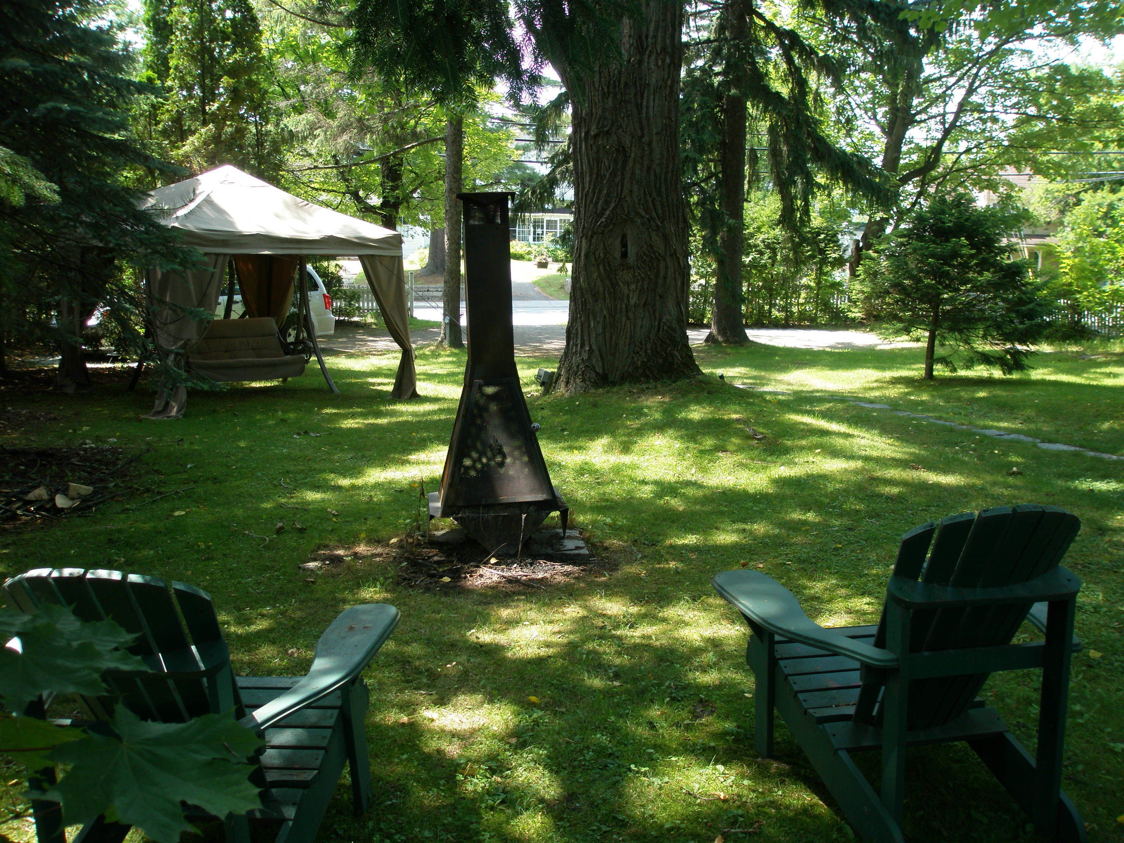 A backyard with a fire pit, two Adirondack chairs, and a tent.