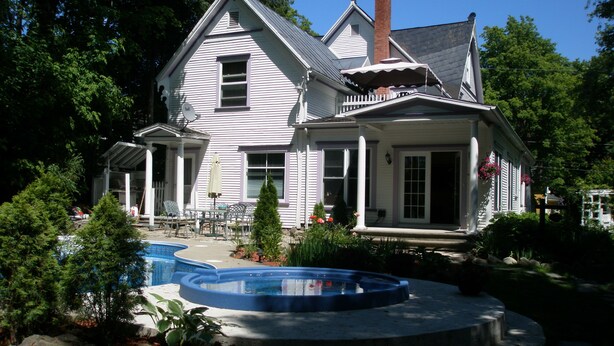 A two-story house with a large front porch, a swimming pool, and a well-maintained garden.