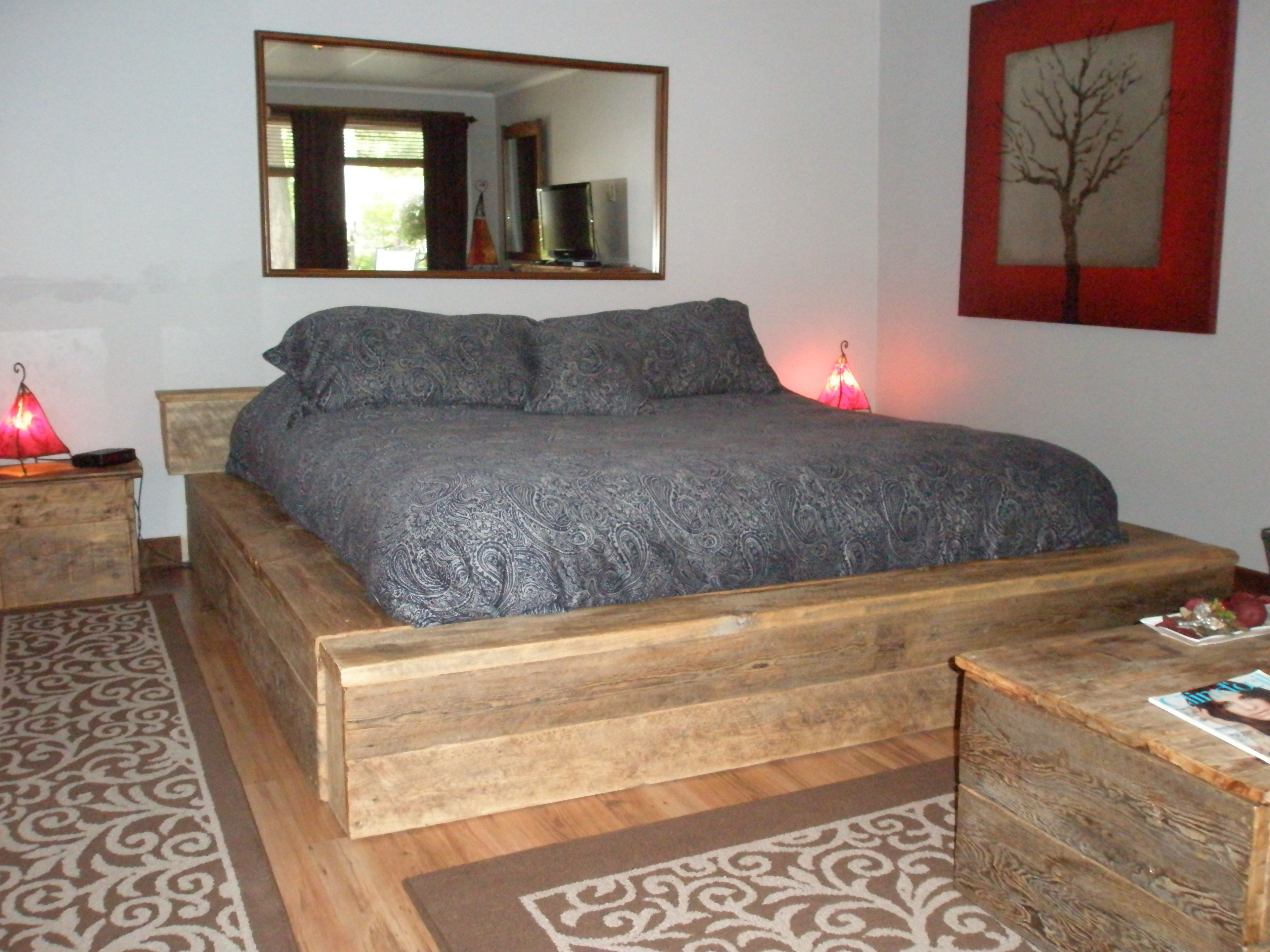 Un dormitorio con cabecera de cama de madera, un espejo grande sobre la cama y un cuadro de un árbol rojo en la pared.