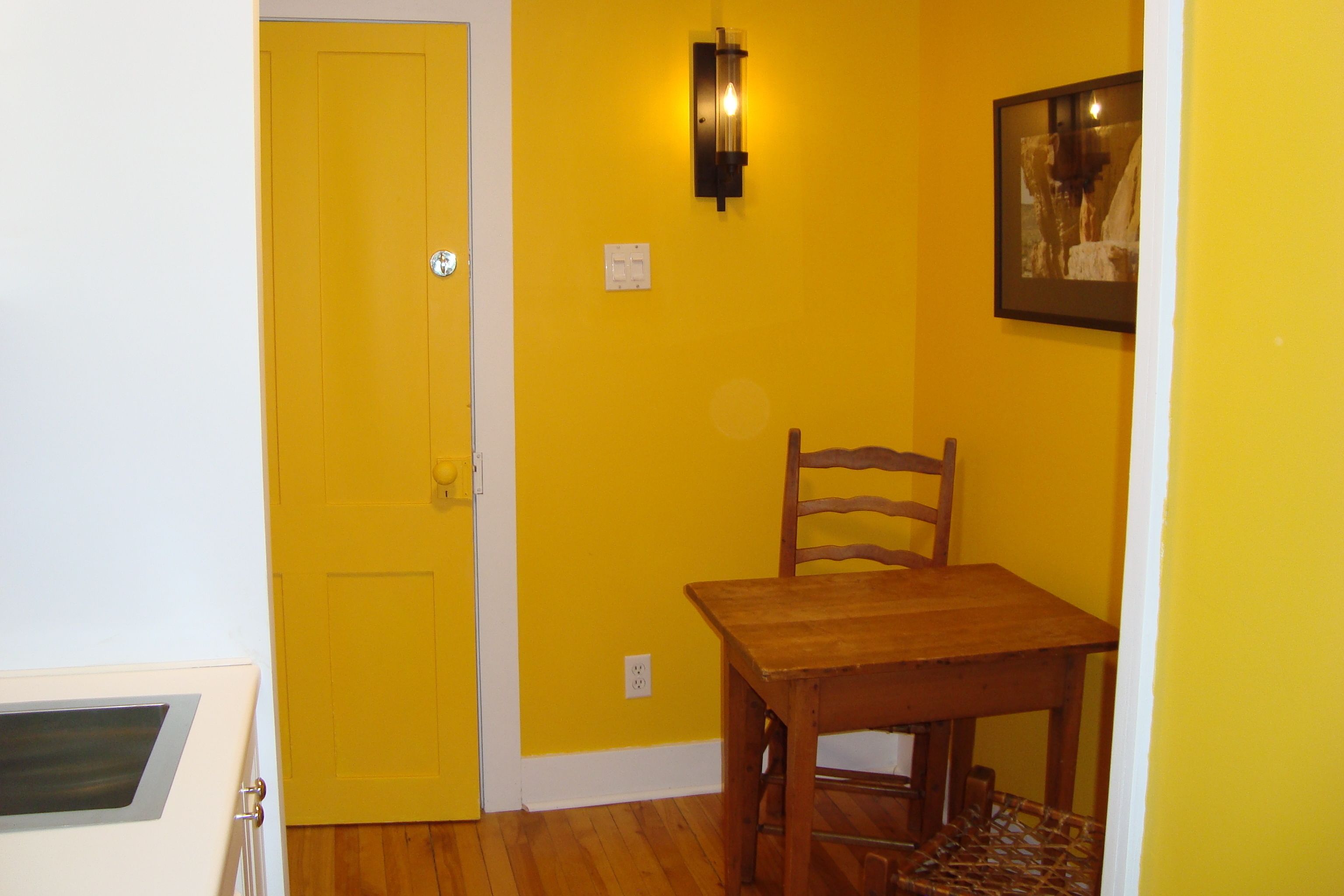 Una habitación con una pared amarilla, una mesa de madera y una silla.