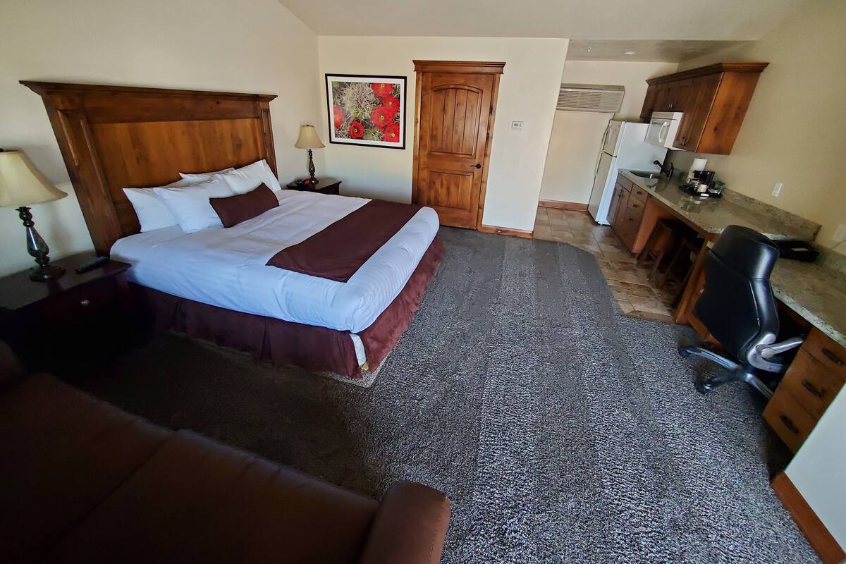 Ein Hotelzimmer mit einem großen Bett, einem Schreibtisch, einem Stuhl, einer Lampe und einem Bild an der Wand.