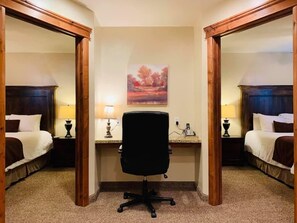 A hotel room with two beds, a desk with a chair, and a painting on the wall. - CB&M Executive Suites (Roosevelt)