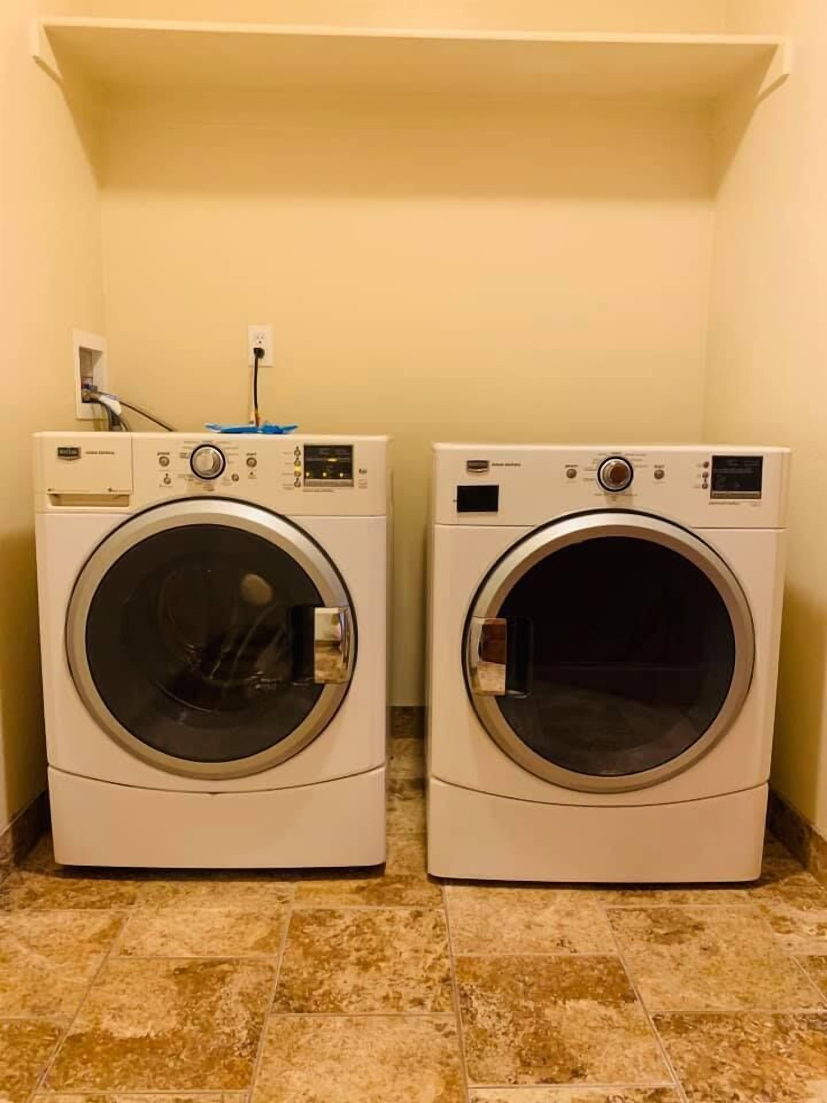Two front-loading washing machines in a laundry room with tiled flooring and a white wall.