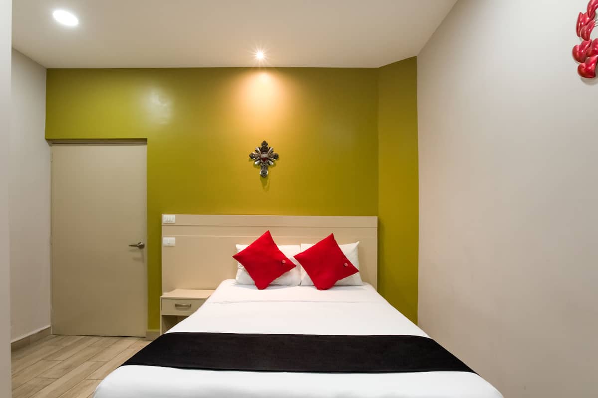 A hotel room with a bed, a nightstand, a wall-mounted light, and a door.
