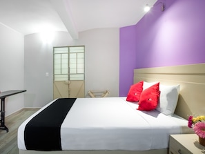 A neatly made bed with white and black bedding, red and white pillows, and a small table with a vase of flowers beside it. - Hotel El Andariego (Oaxaca)