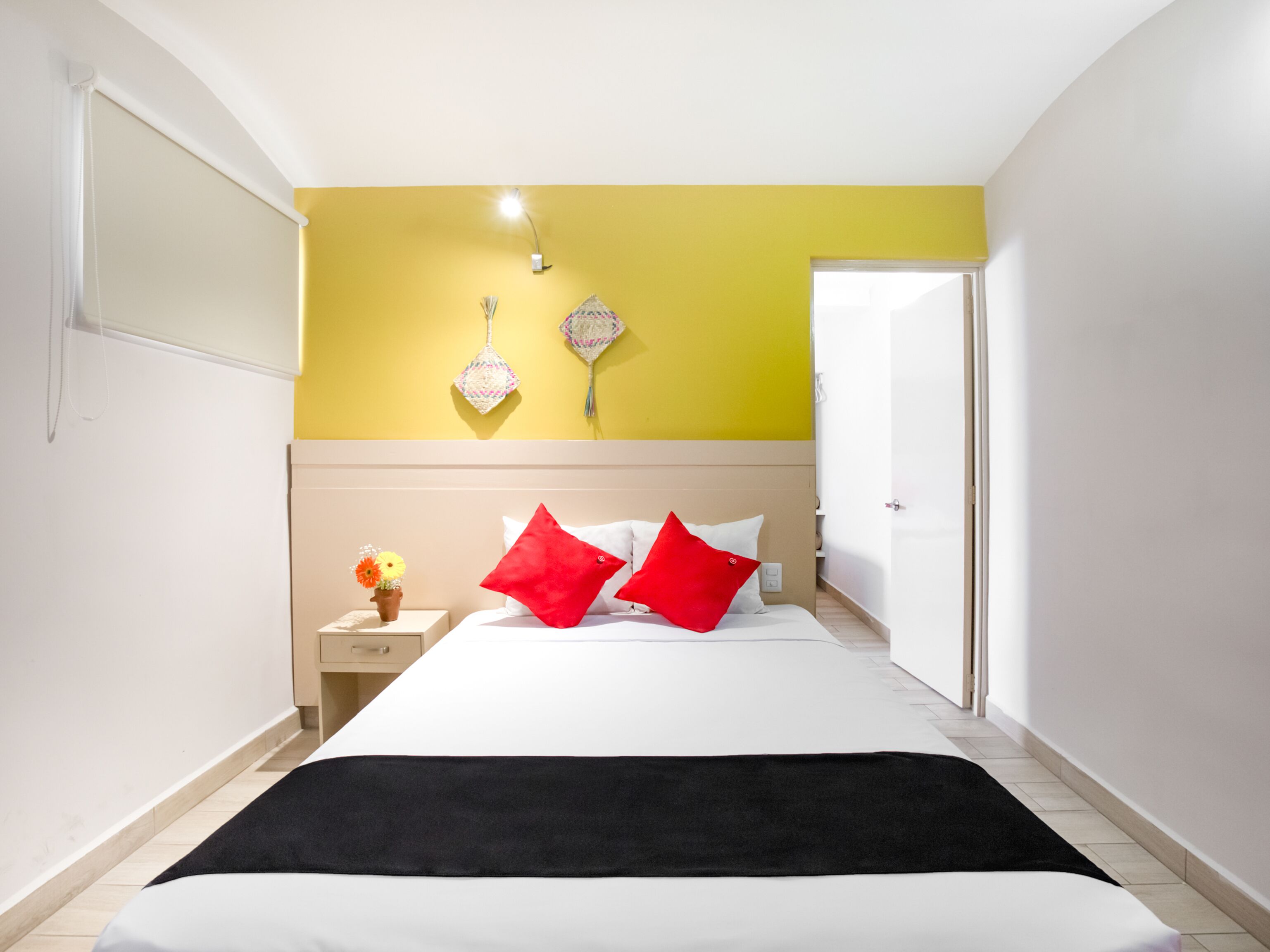 Habitación de hotel con cama, mesita de noche, lámpara y luz empotrada en la pared.