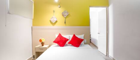 Habitación de hotel con cama, mesita de noche, lámpara y luz empotrada en la pared.