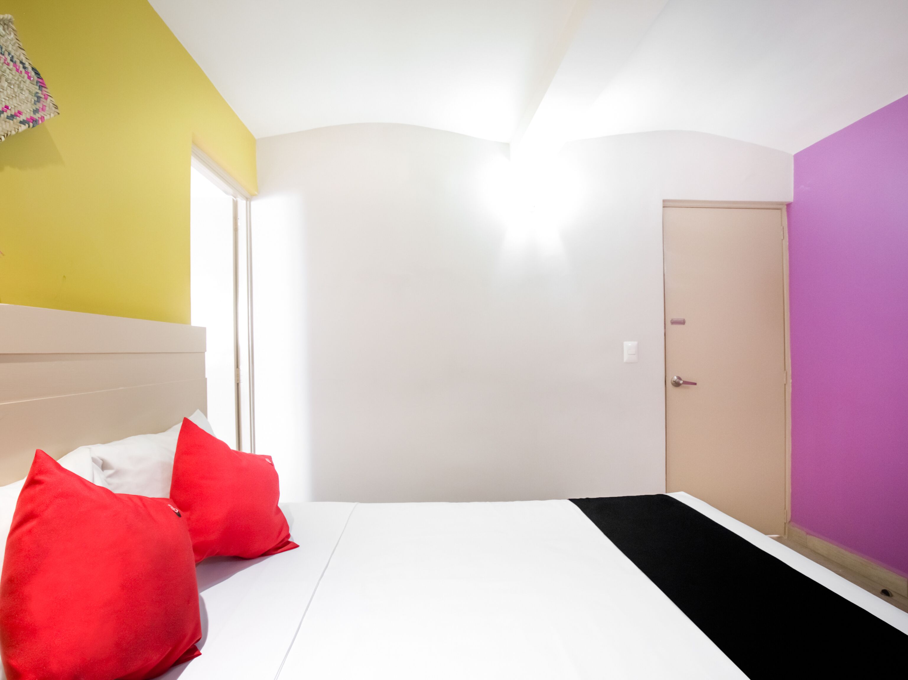 A bedroom with a bed, two red pillows, a white mattress, a door, and a wall with a yellow and purple color scheme.