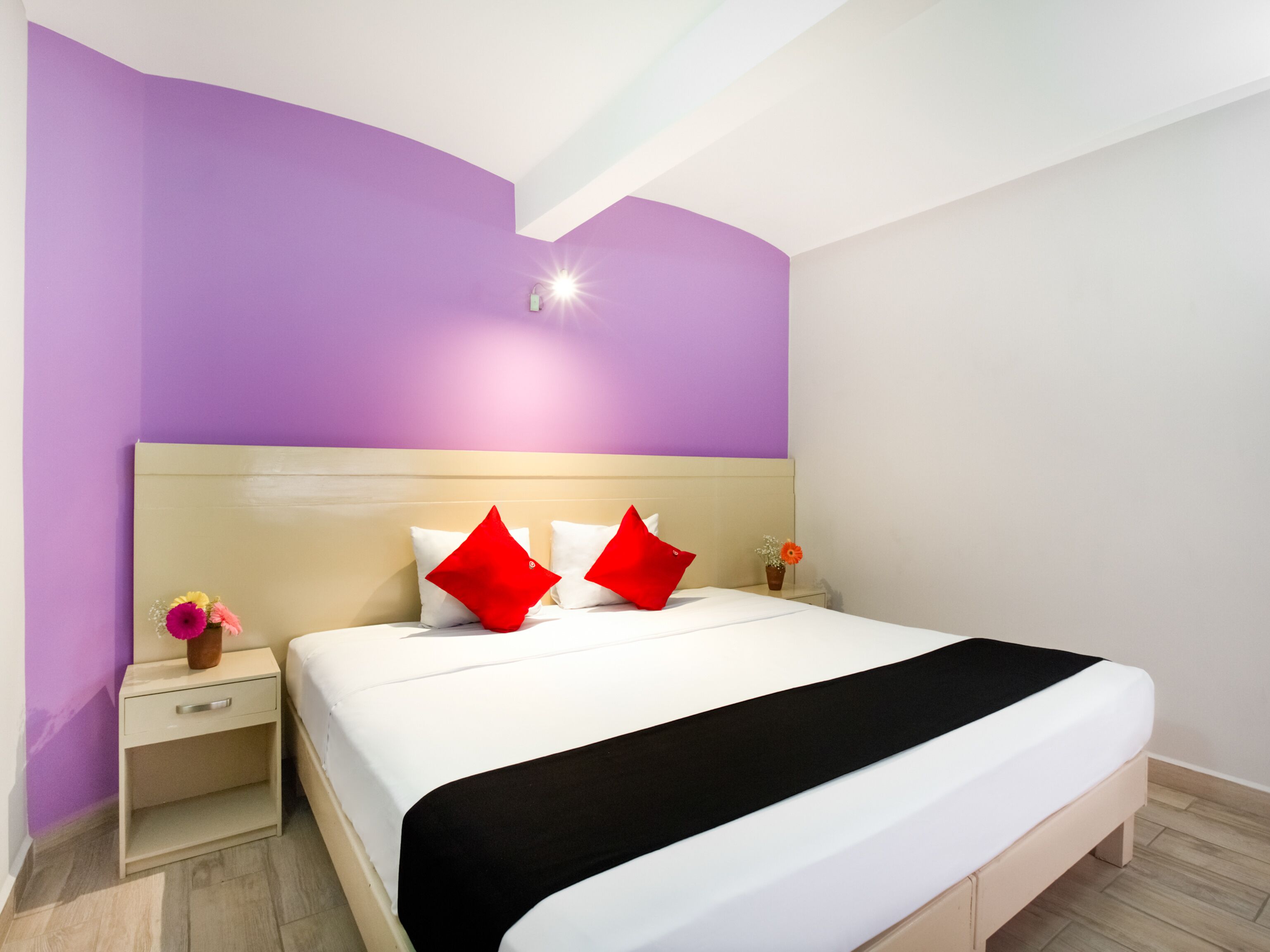 A modern hotel room with a large bed, a nightstand, and a vase of flowers.
