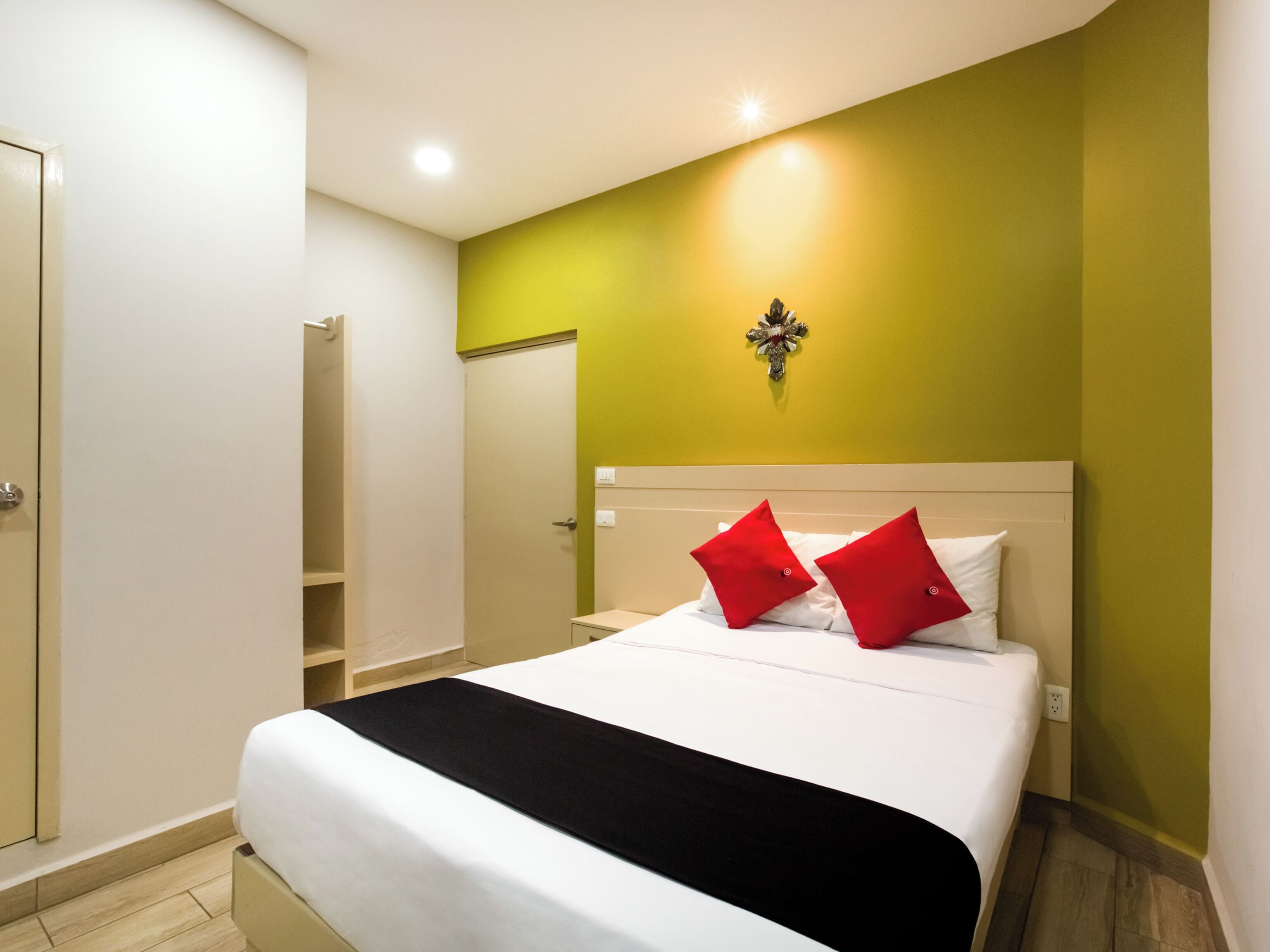 A hotel room with a bed, a nightstand, a wall-mounted light, and a door.