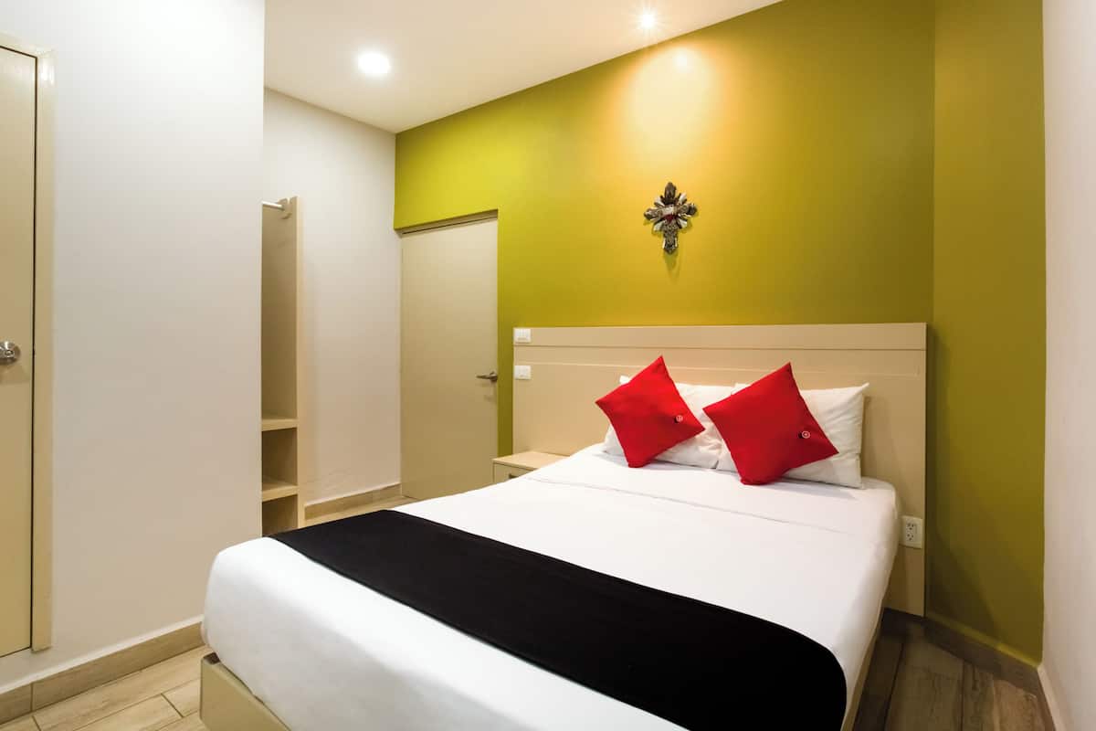 A hotel room with a bed, a nightstand, a wall-mounted light, and a door.